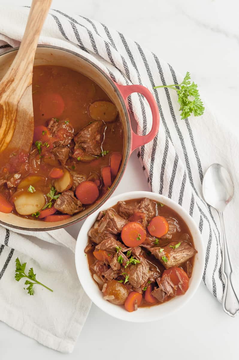 bowl of beef stew next to beef stew in a dutch oven