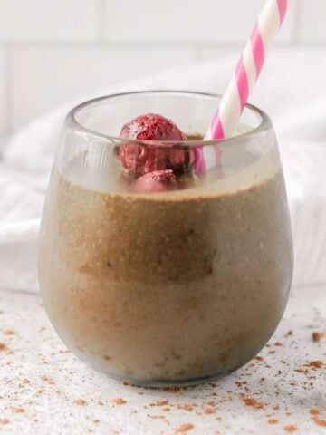 close up of chocolate smoothie with cherries in a glass with a straw.