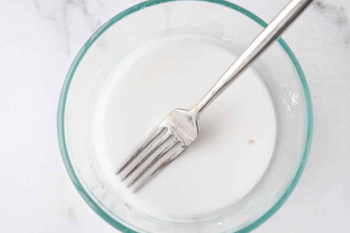 arrowroot and water in a glass bowl with a fork on a white background.