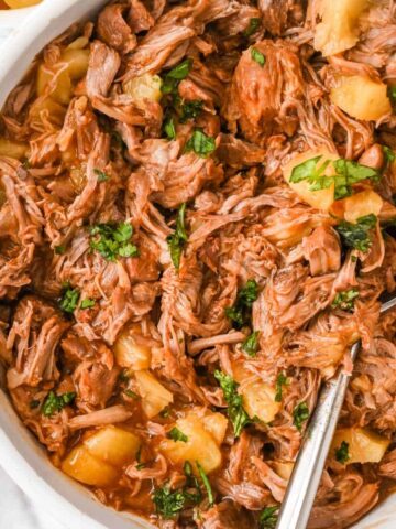 close up view of pineapple pulled pork topped with cilantro with a spoon in a white bowl.