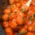 close up shot of meatballs in a crock pot with a wooden spoon.