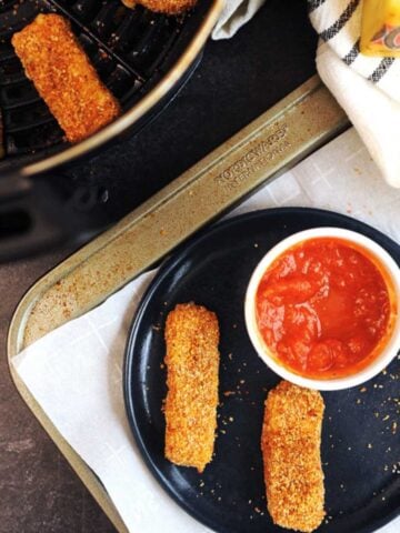 two keto cheesesticks on a plate with tomato sauce.
