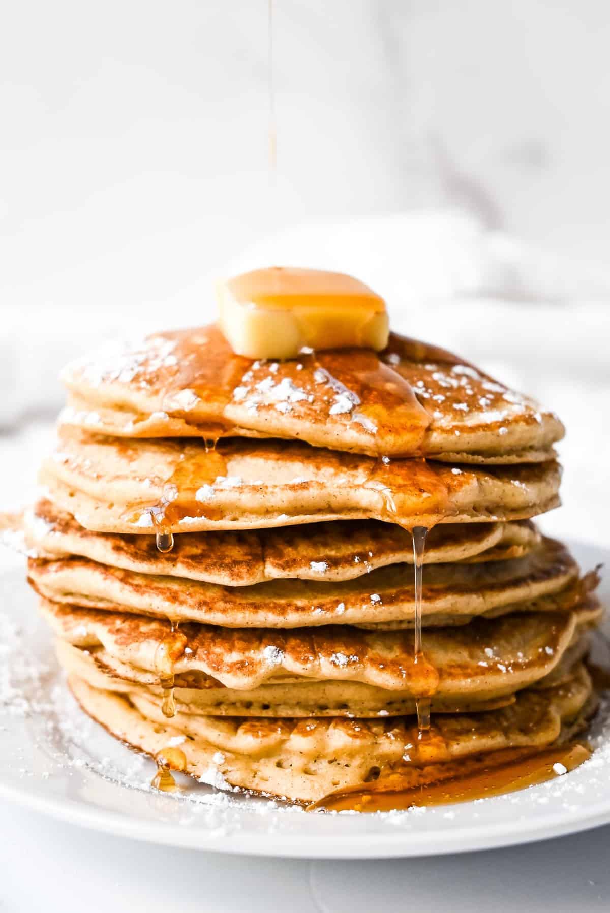 stack of oat flour pancakes with maple syrup, butter and powdered sugar.
