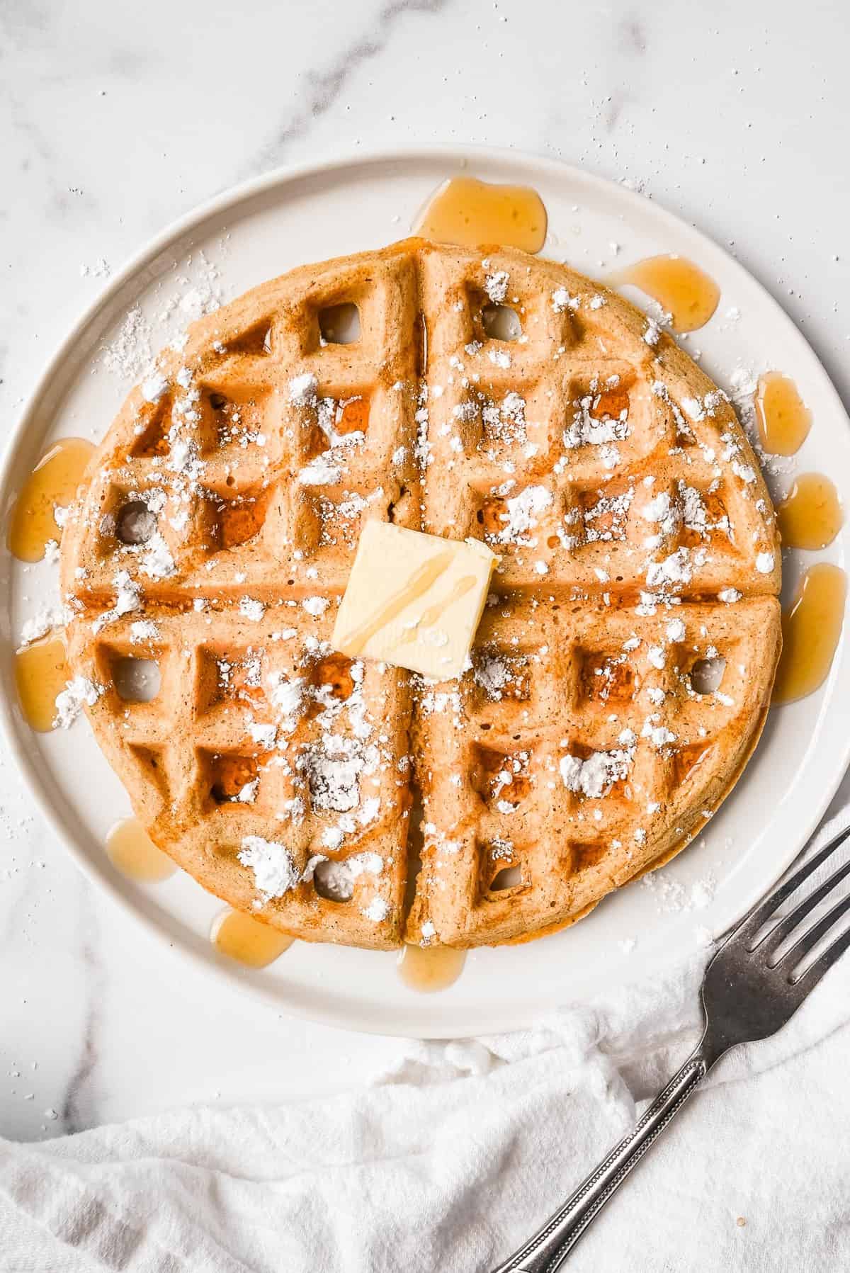 oat flour waffle on a plate topped with butter, maple syrup and powdered sugar