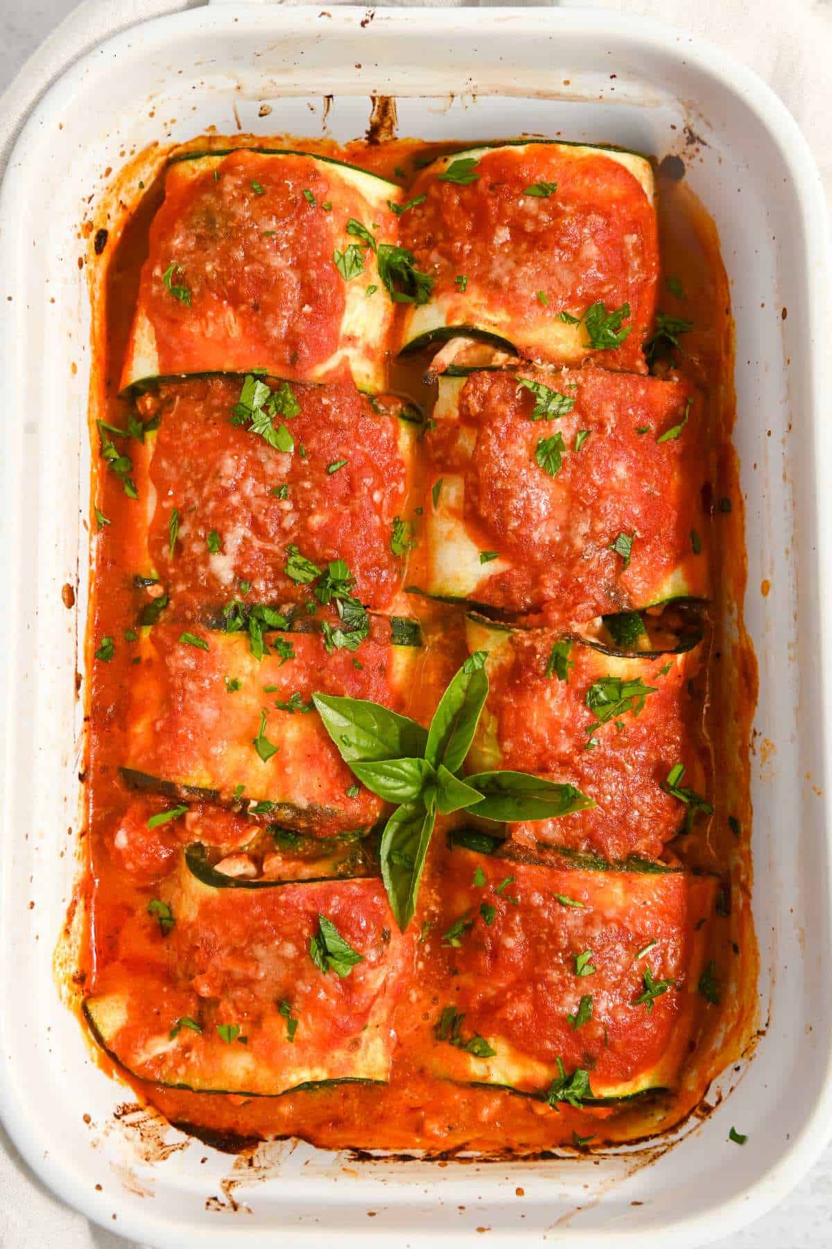white pan with eight zucchini rollups topped with sauce and basil.