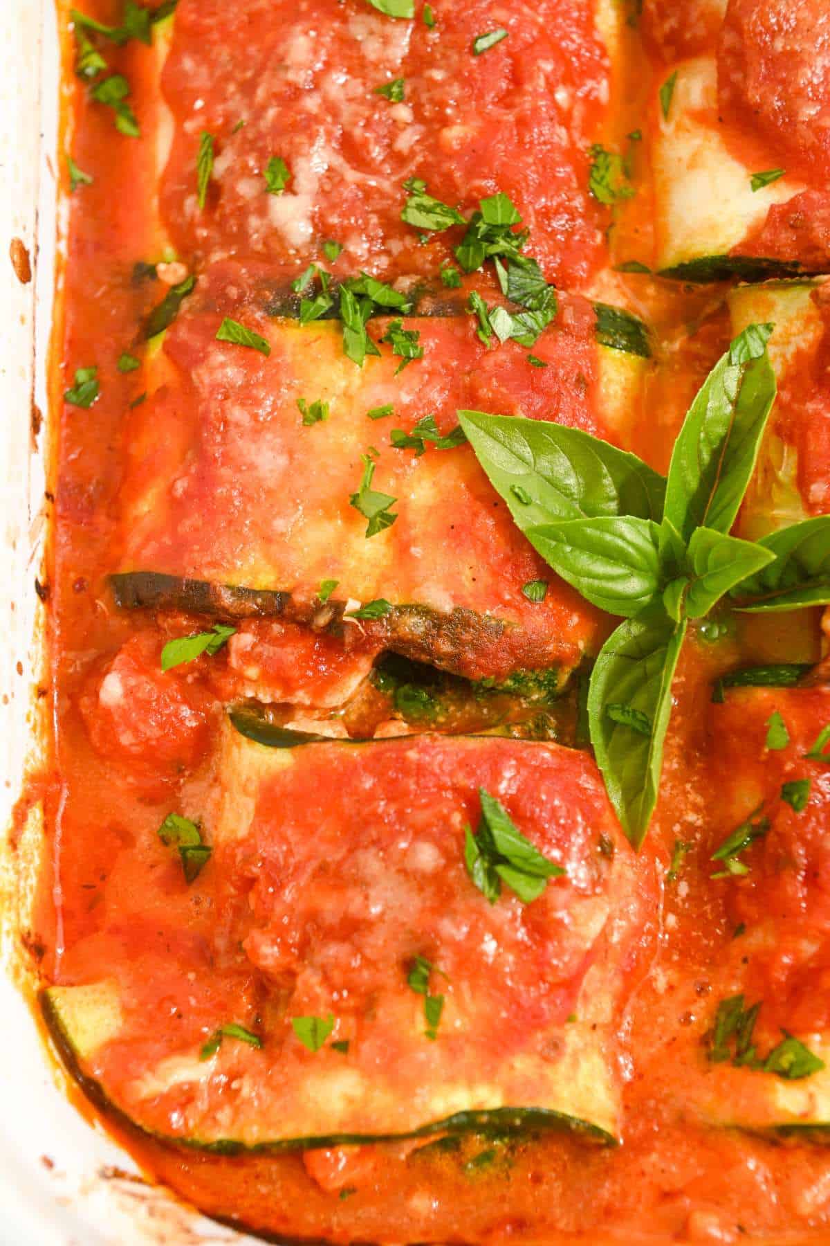 close up shot of three zucchini rollups topped with sauce and basil.