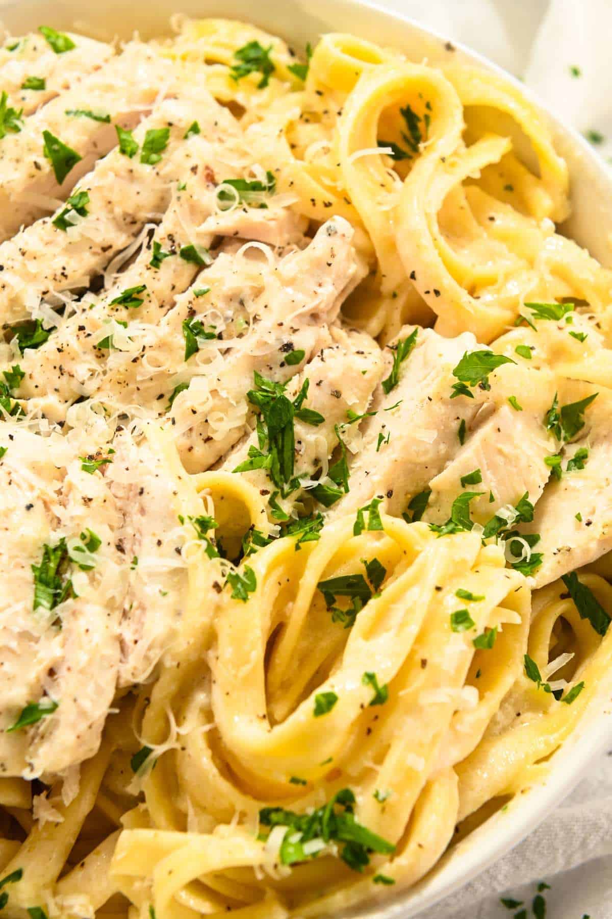 Healthy crockpot chicken alfredo in a white bowl topped with parsley and parmesan cheese.
