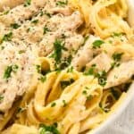 close up photo of fettuccine alfredo with chicken topped with parsley and Parmesan cheese.