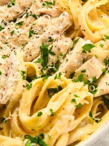 close up photo of fettuccine alfredo with chicken topped with parsley and Parmesan cheese.
