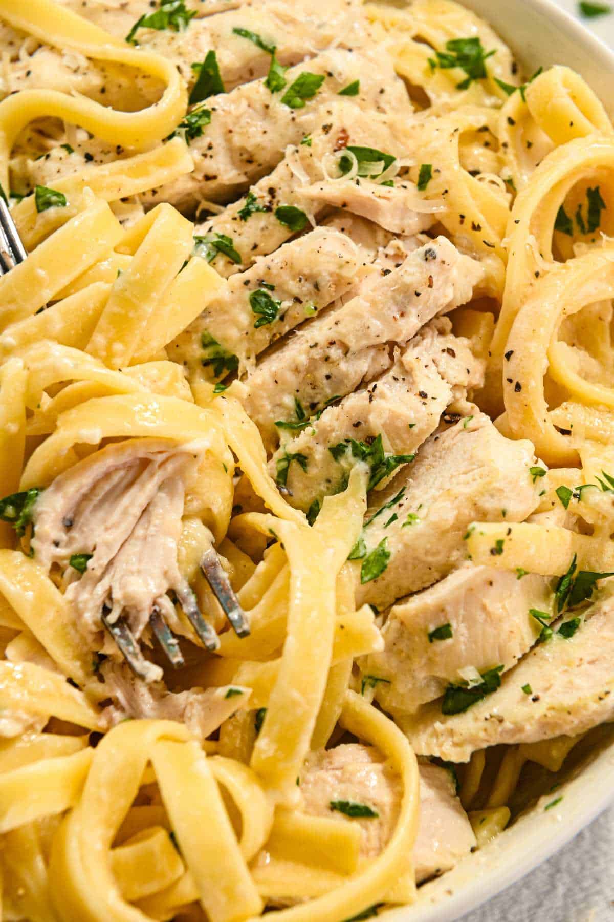 Sliced chicken on top of healthy slow cooker fettuccine alfredo.