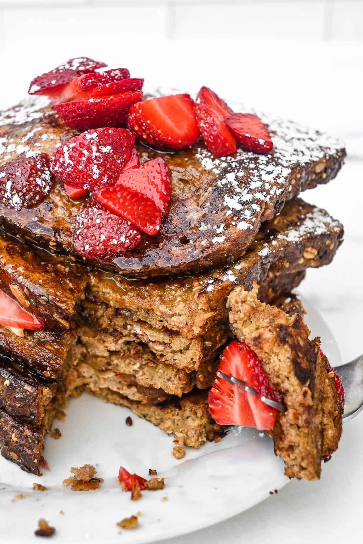 cut out section of daves killer bread french toast with strawberries on a fork on a white plate.