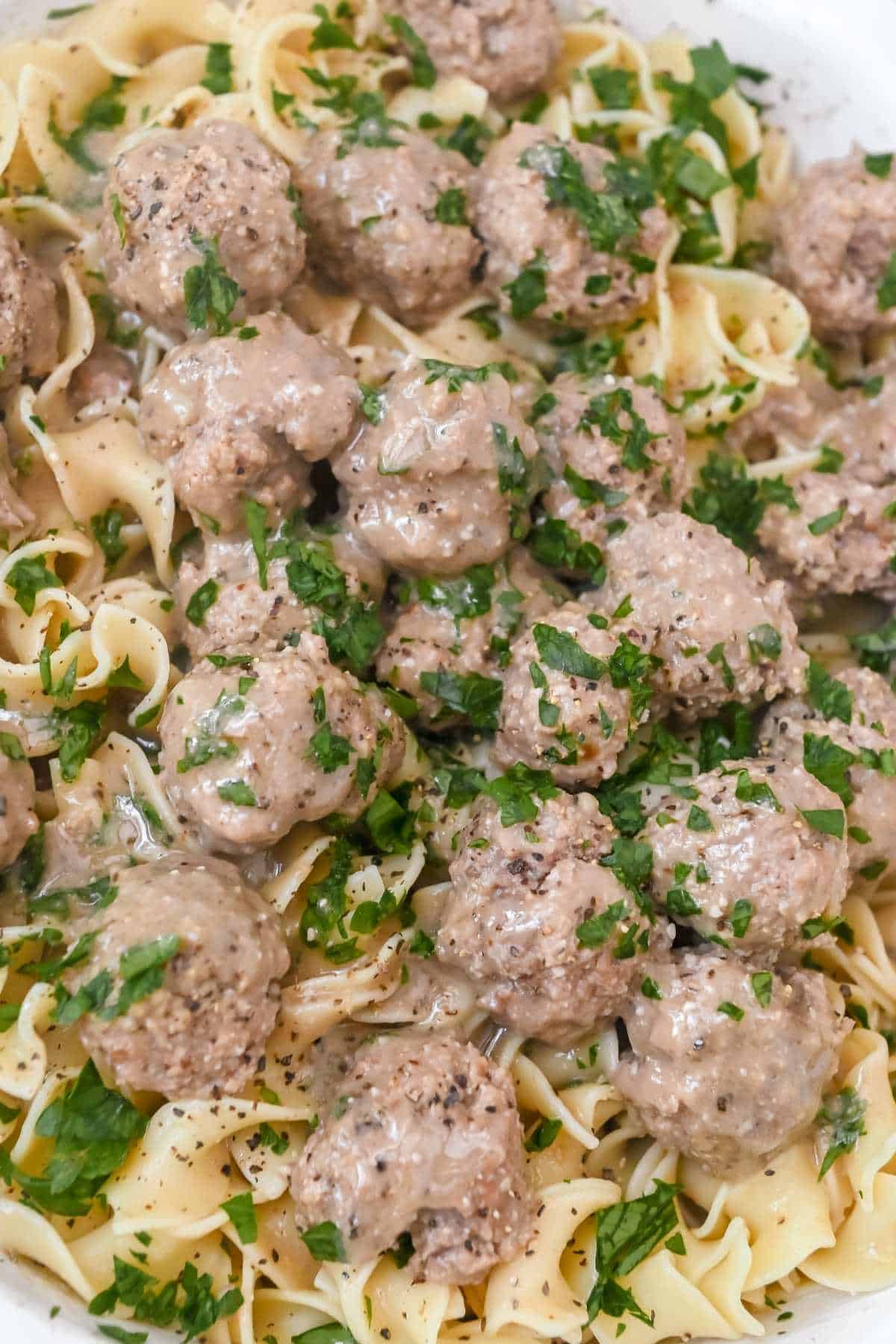 close up shot of swedish meatballs over egg noodles topped with parsley.