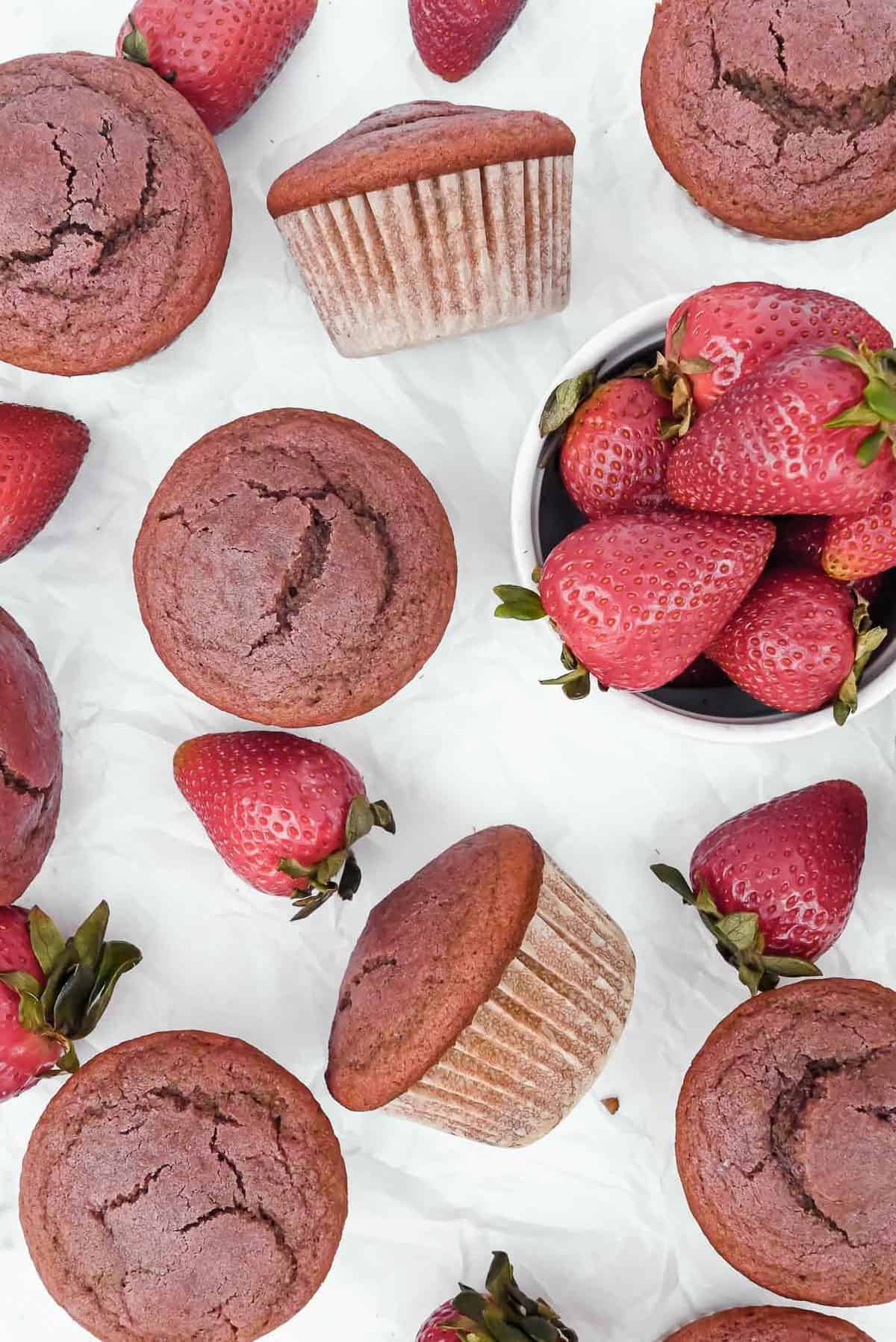 strawberry yogurt muffins on parchment paper with a bowl of strawberries.