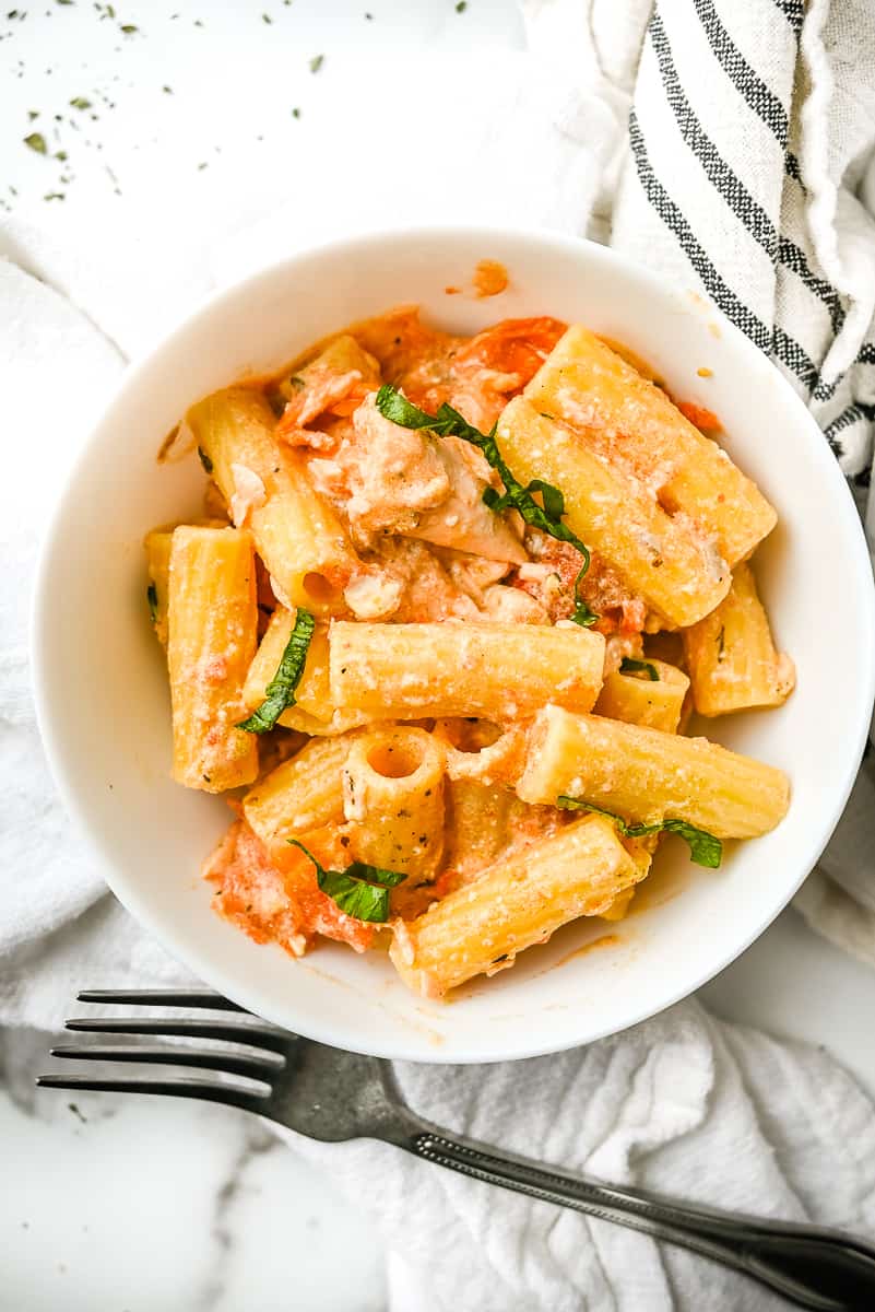 bowl of feta baked pasta with salmon on a white background with a towel.