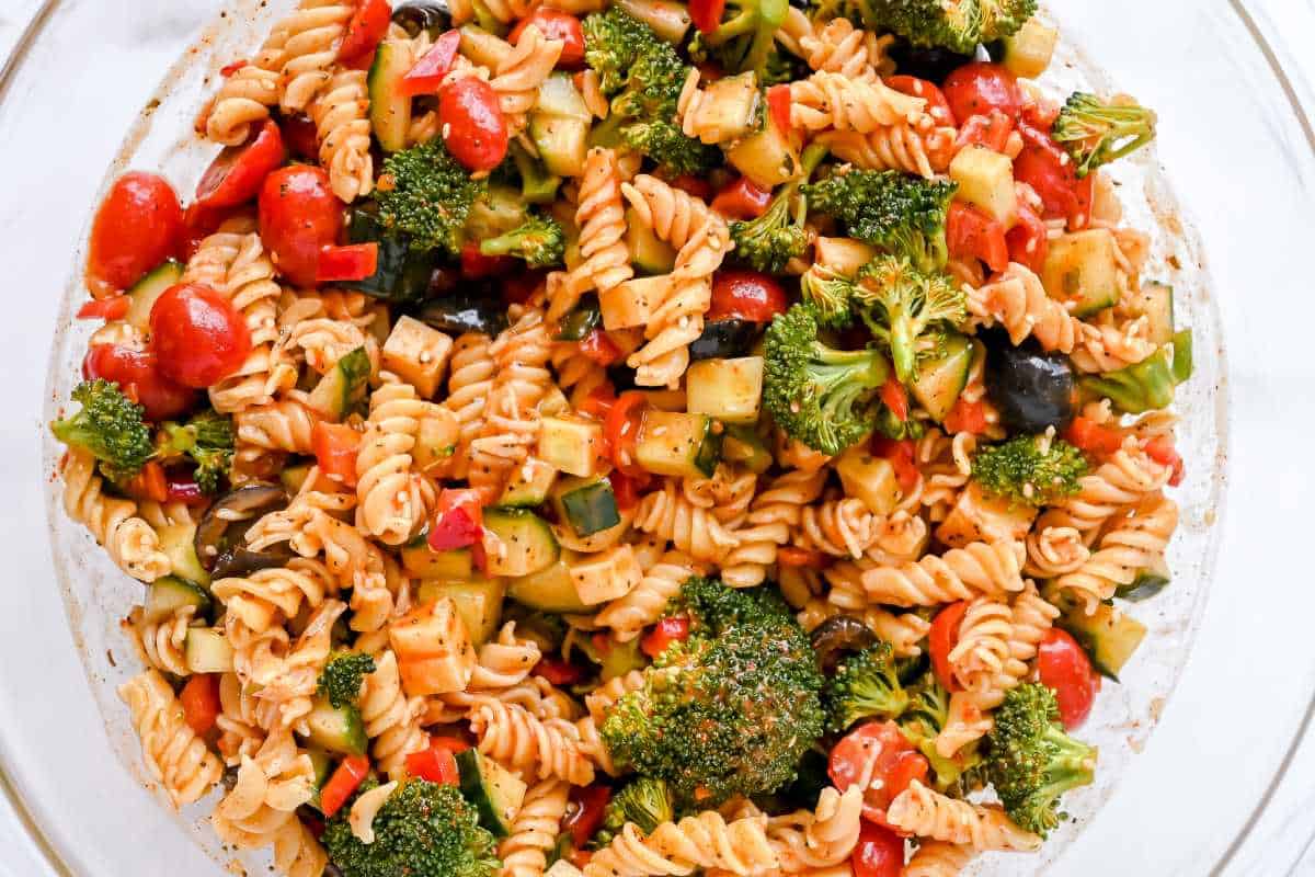 combined pasta salad ingredients in a glass bowl on a white background.