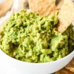 guacamole in a white bowl with two tortilla chips.