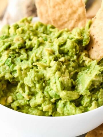 guacamole in a white bowl with two tortilla chips.