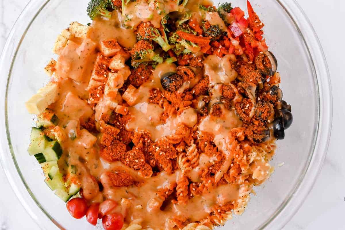 gluten-free pasta salad ingredients with dressing in a glass bowl on a white background.