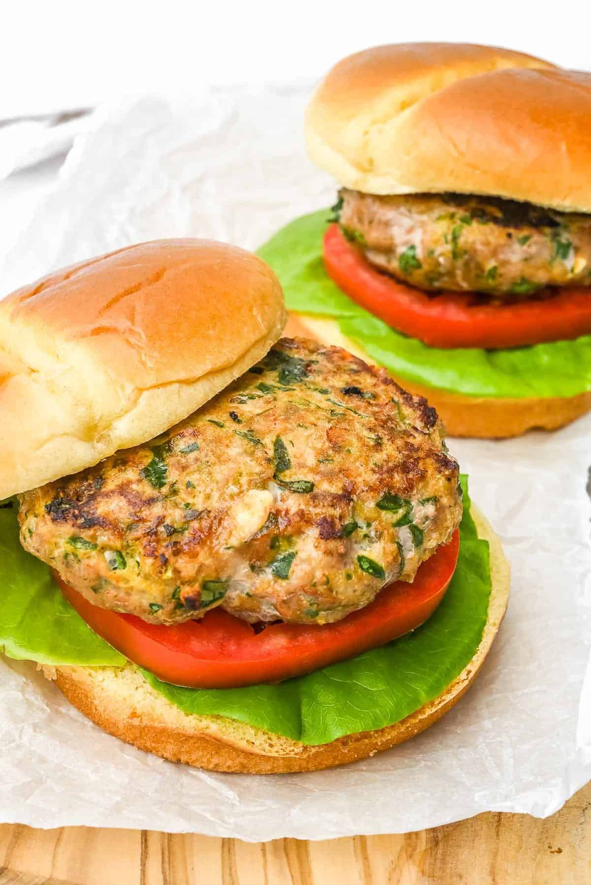 two healthy turkey burgers on a piece of parchment paper with one bun offset to show patty.