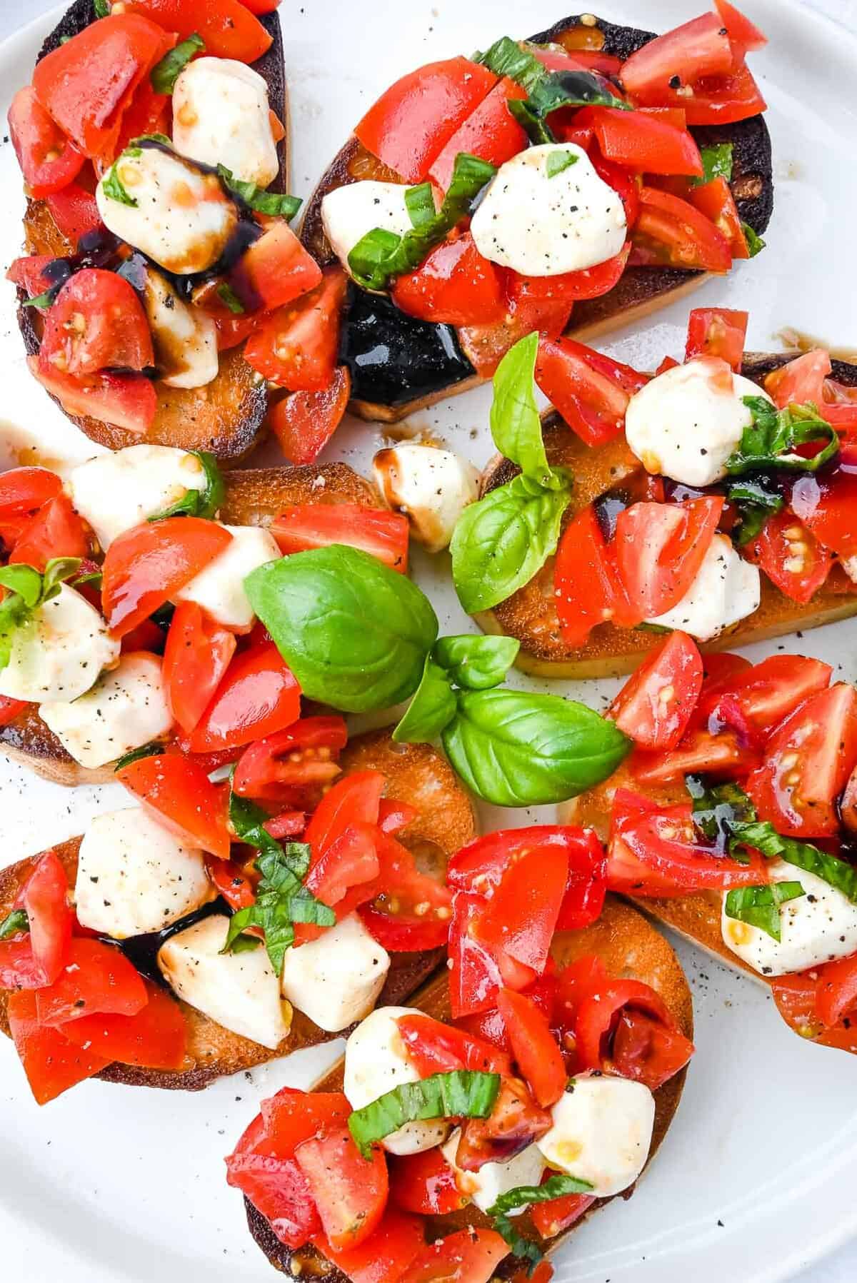 bruschetta on a white plate topped with cheese and basil.