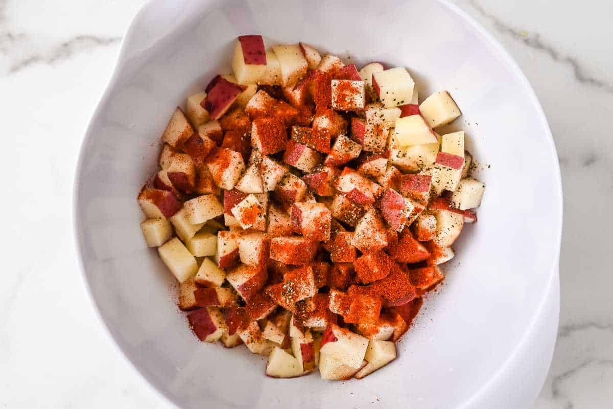 potatoes and seasoning in a white bowl on a white background.