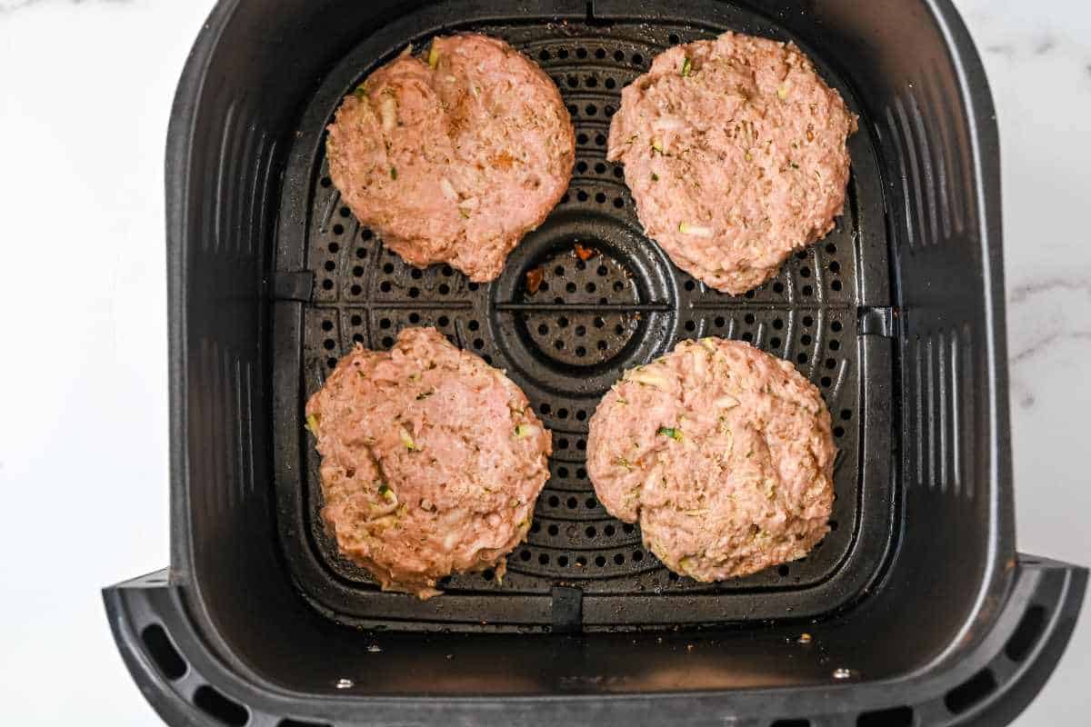 four raw turkey burgers in a black air fryer basket.