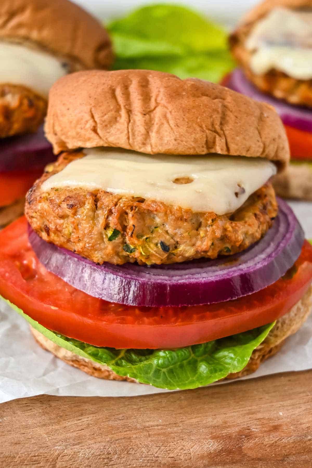 close up shot of air fryer turkey burgers topped with swiss cheese and with a bun, lettuce, tomato, and onion.