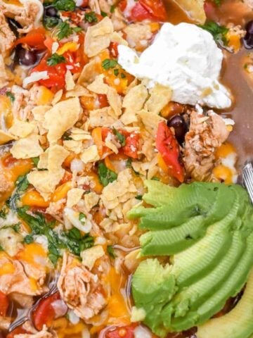close up of 5-ingredient chicken tortilla soup topped with avocado slices and sour cream and with a silver spoon.