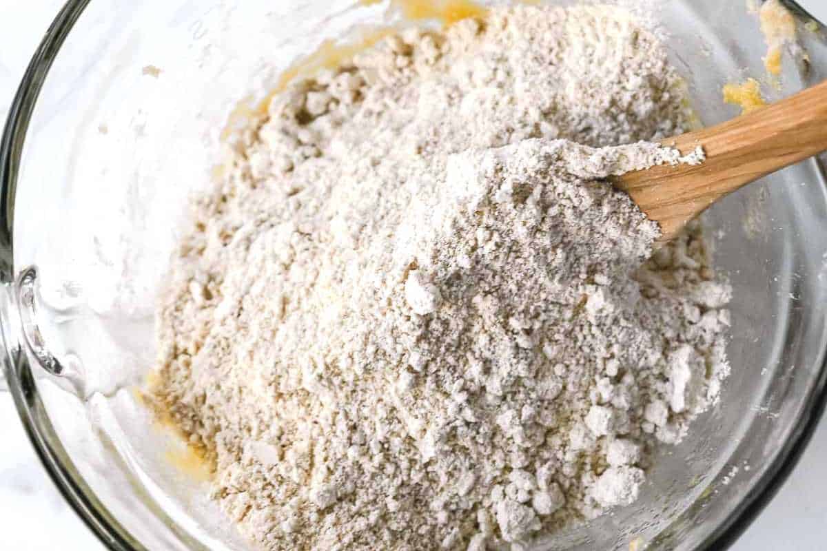 dry cookie ingredients on top of wet ingredients in a bowl with a wooden spoon.