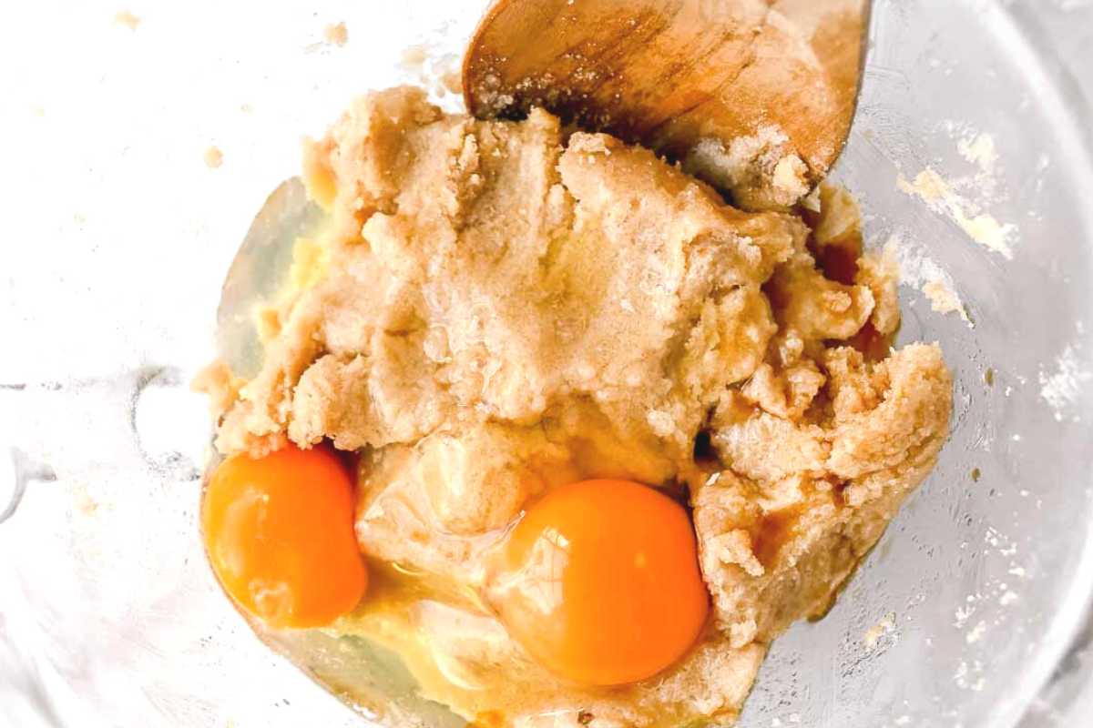 eggs and wooden spoon in cookie ingredients in a bowl.