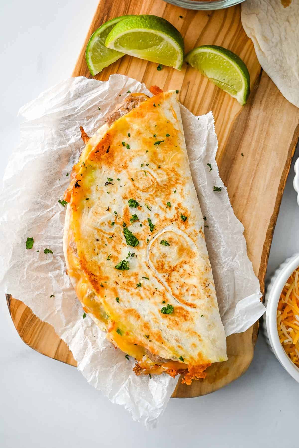 full carne asada quesadilla on a piece of parchment paper on a wooden board with limes.
