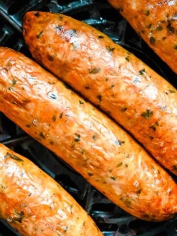close up shot of air fryer chicken sausage in a black air fryer basket.
