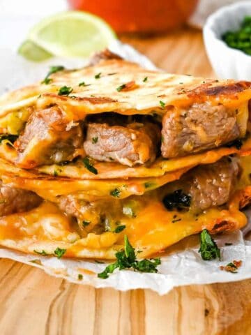 stack of carne asada quesadilla pieces on a wooden board.