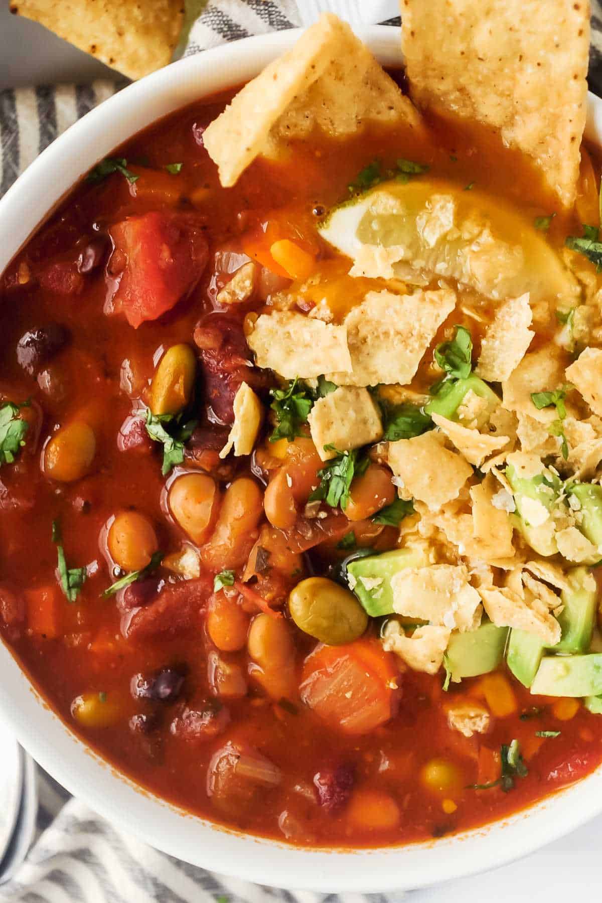top view of chili in a white bowl topped with tortilla chips and avocado.