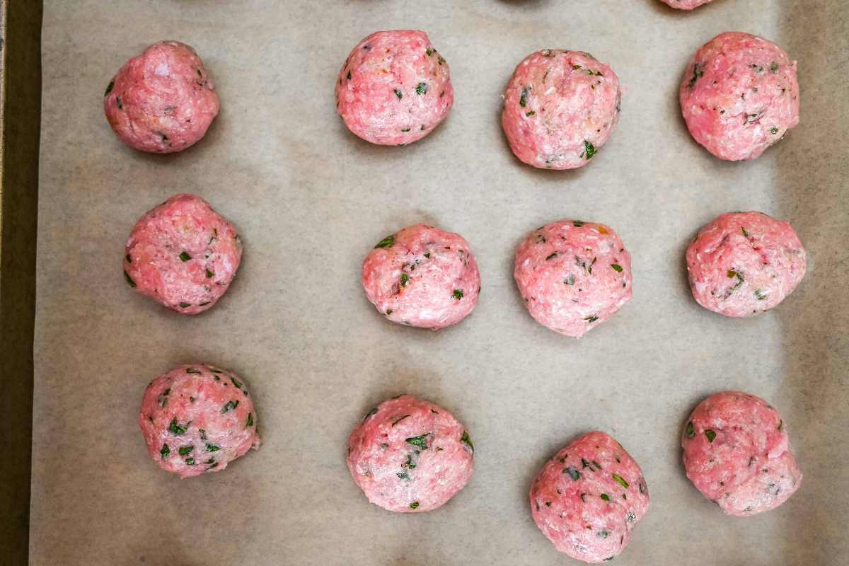 uncooked meatballs on a baking sheet.
