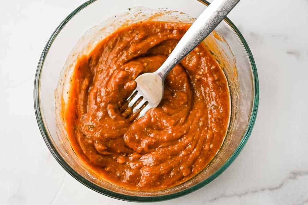 close up shot of wing sauce in a glass bowl with a fork in it.