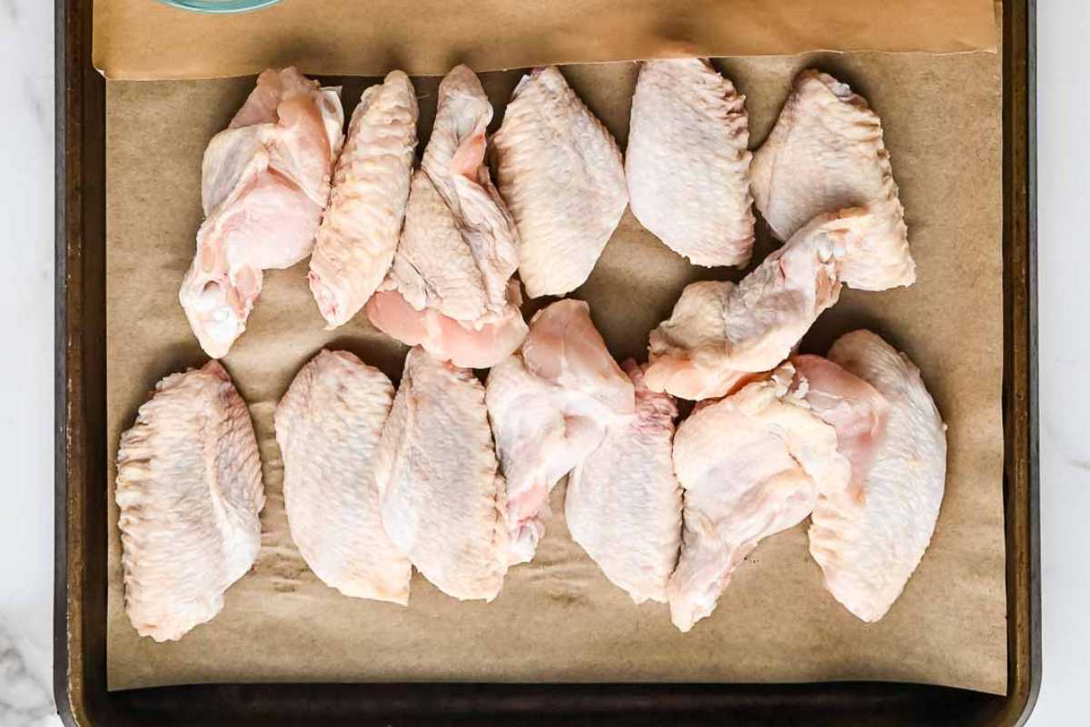 raw chicken wings on parchment paper on a baking sheet.