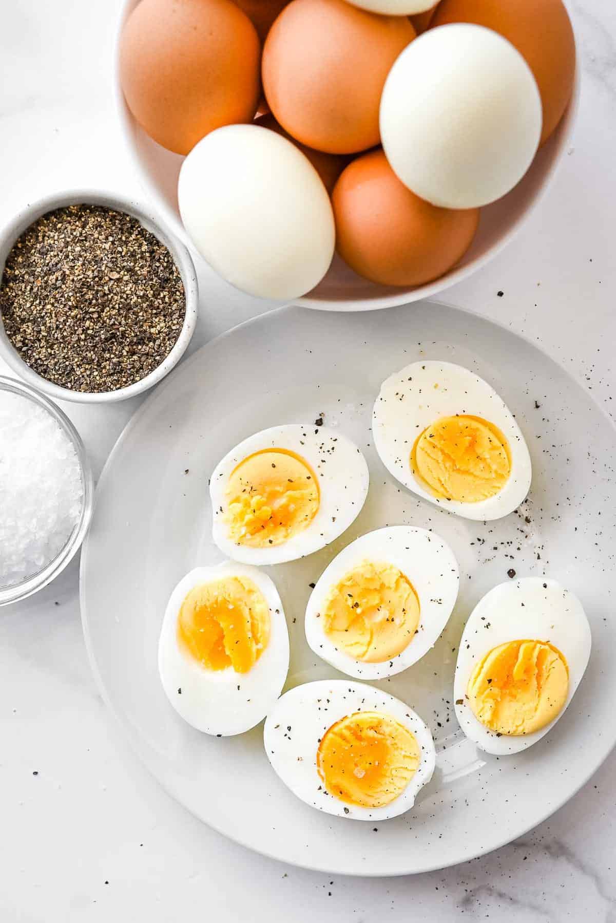 plate of ninja foodi hard boiled eggs with salt and pepper and bowl of raw eggs next to it.