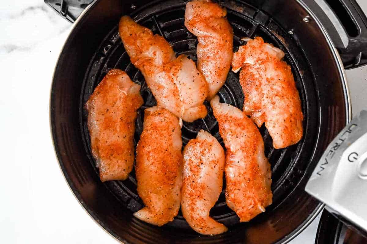 raw chicken tenders in an air fryer basket.