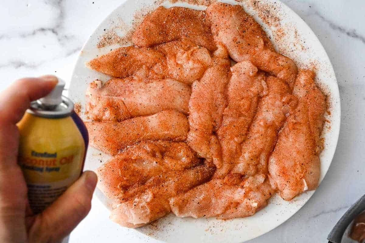 view of hand spraying chicken tenders with cooking spray.
