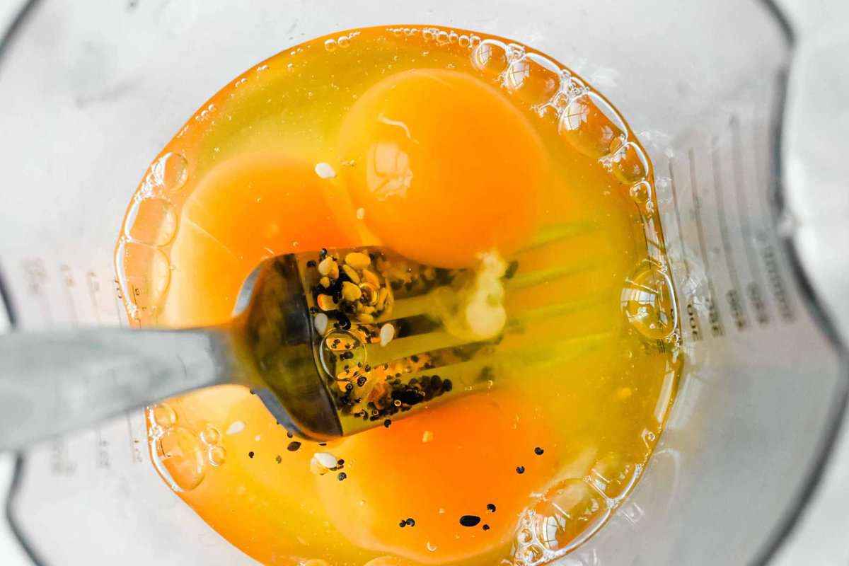 eggs in a plastic cup with seasoning and a fork.