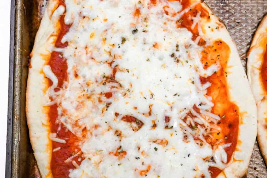 close up of cooked naan bread pizza on a sheet pan.