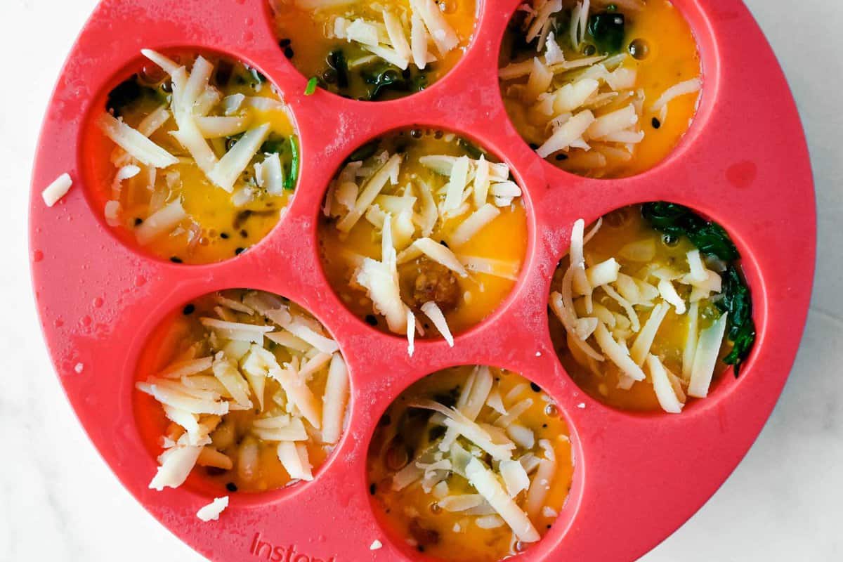 uncooked egg bites in a red silicone mold topped with cheese.
