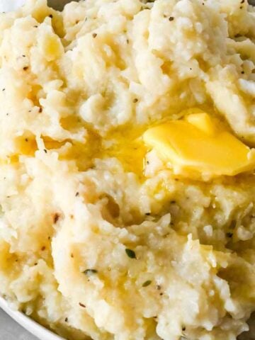 closeup of mashed potatoes and cauliflower topped with butter.