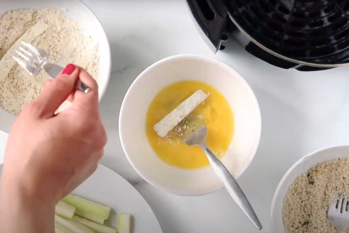 hand breading air fryer zucchini sticks with 3 bowls.