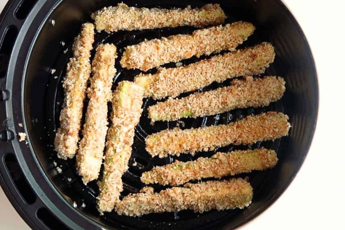 breaded zucchini sticks in a black air fryer basket.