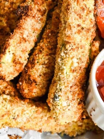 close up of zucchini sticks with breading with dipping sauces on the side.