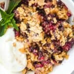 close up shot of blackberry cobbler with ice cream in a white bowl topped with mint.