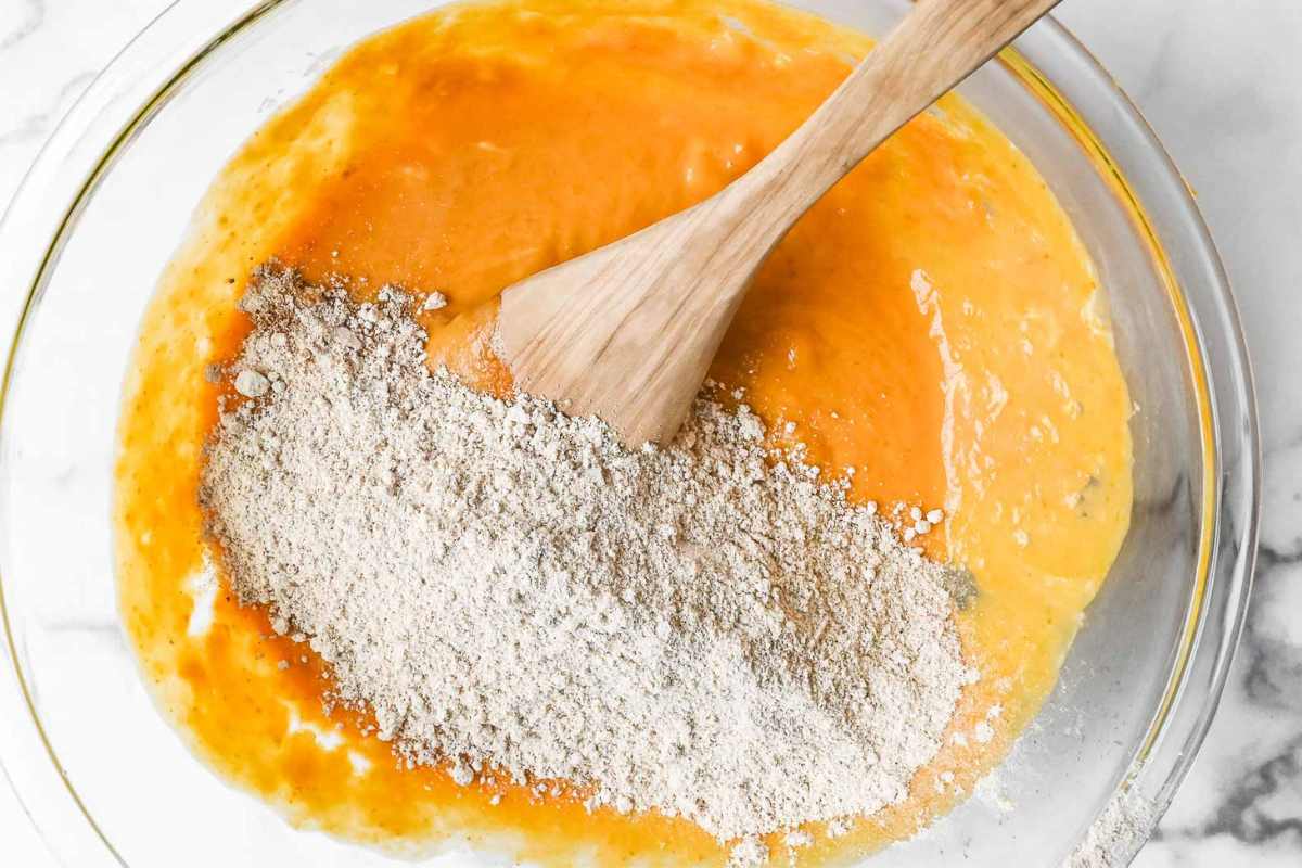 glass bowl with pumpkin banana muffin ingredients and a wooden spoon.