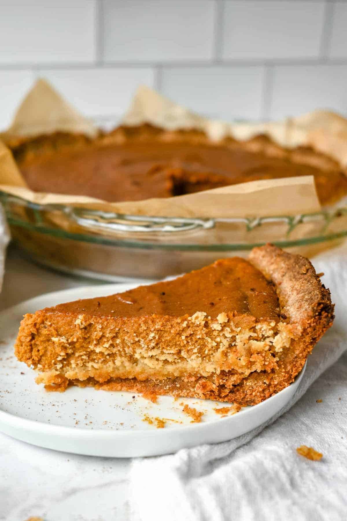 slice of pumpkin pie on a white plate in front of the full pie.